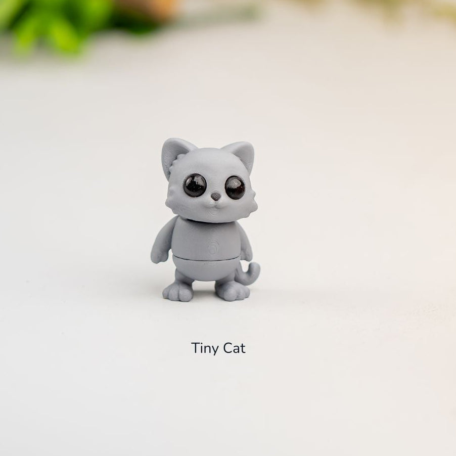 Gray cat figurine on a light surface with decorative plants in the background