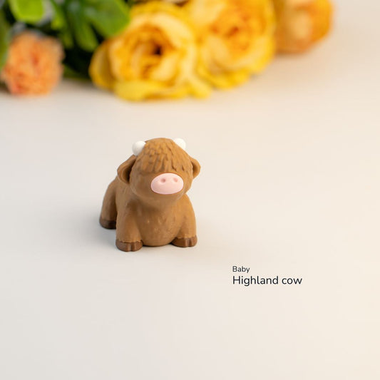 Small brown Highland cow figurine on a light surface with flowers in the background