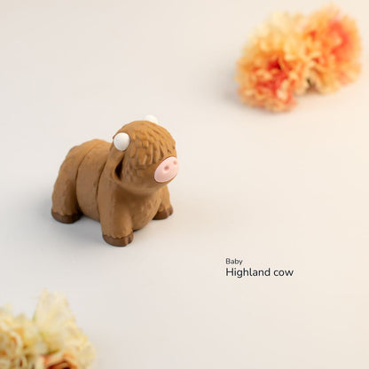 Small brown Highland cow figurine on a light background with decorative flowers.