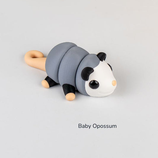 Toy opossum with a gray body, black ears and eyes, and beige tail on a light gray background.