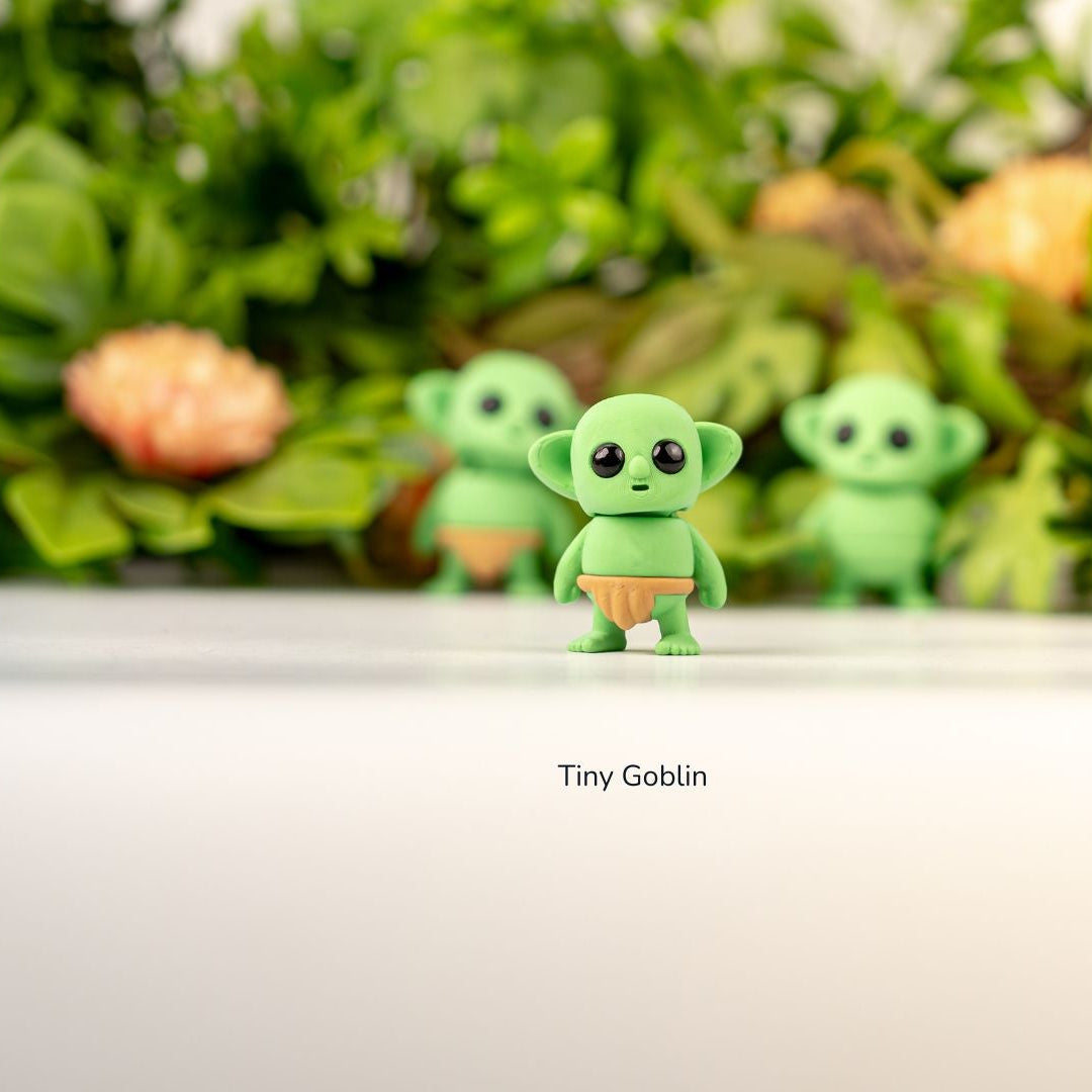 Green figurines with 'Tiny Goblin' text on a white surface with a blurred natural background